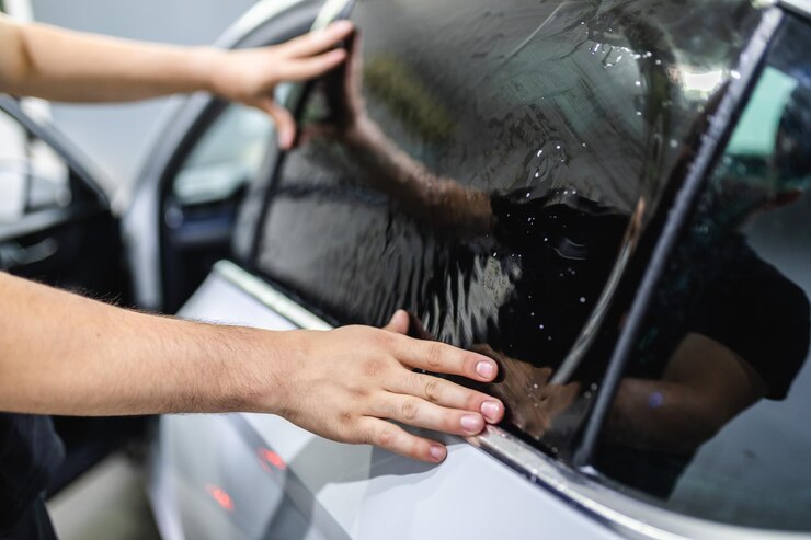 Autotönung - Arbeiter, die Tönungsfolie auf Autofenster aufbringen.