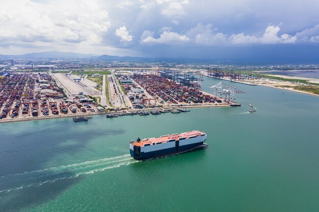 Autotransporter, der auf der grünen See- und internationalen Schiffscontainerhafenhintergrundluftansicht segelt