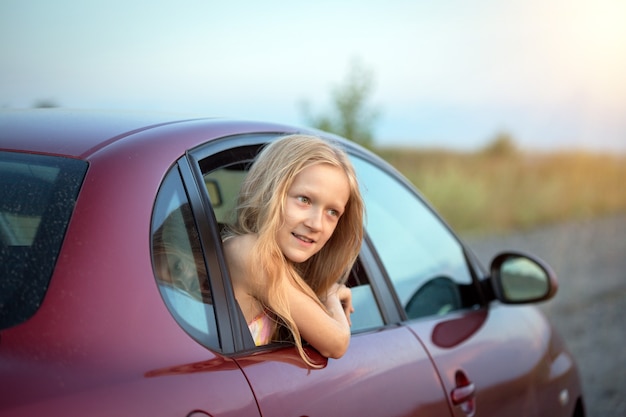 Autotravel com crianças. menina sorridente feliz olhando pela janela do carro e o pôr do sol ao fundo