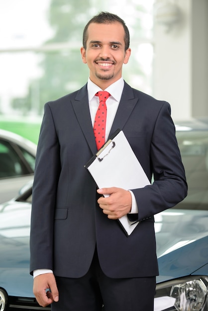 Autoverkäufer, der an der Verkaufsstelle steht und Auto zeigt.