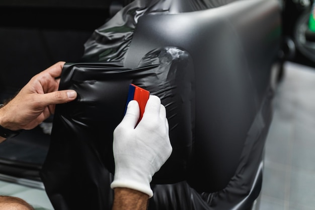 Autoverpackungsspezialist, der Vinylfolie oder -folie auf das Auto legt. Selektiver Fokus.