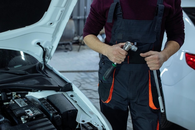 Autowerkstatt. Ein Automechaniker steht mit einem Werkzeug in der Hand neben dem Auto. Technische Inspektion des Fahrzeugs.