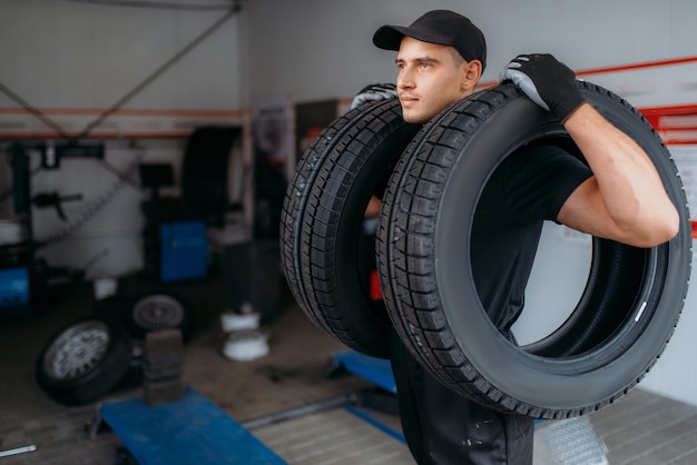 Autowerkstatt in Uniform hält zwei neue Reifen, Reparaturservice. Arbeiter repariert Autoreifen in der Garage, professionelle Autoinspektion in der Werkstatt