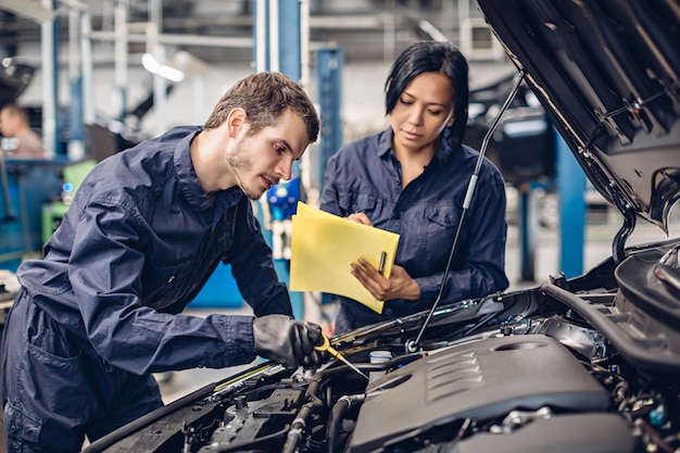 Autowerkstatt. Zwei Mechaniker - Untersuchungsautomotor des Mannes und der Frau