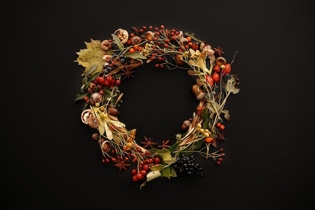 Autumn Wreath Flat Lay Hojas de otoño círculo con bayas nueces bellotas flores hierbas sobre fondo negro vista superior Saludos de temporada Espacio para texto Tarjeta de maqueta de otoño