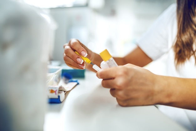 Auxiliar de laboratorio femenina preparando agujas y tubos de ensayo para muestreo de sangre.