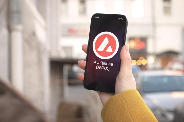 Avalanche AVAX-Kryptowährungssymbol, Logo. Geschäfts- und Finanzkonzept. Hand mit Smartphone, Bildschirm mit Kryptosymbol-Nahaufnahme