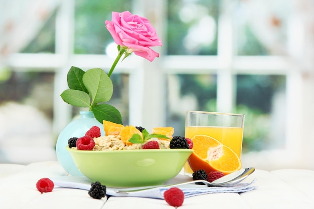 Aveia saborosa com bagas e copo de suco na mesa no fundo da janela