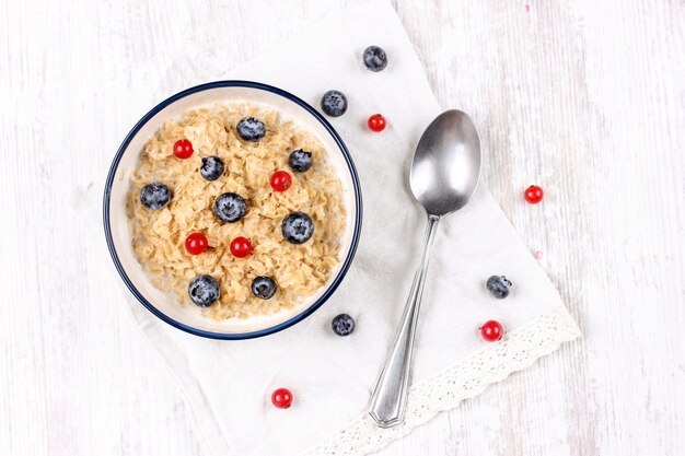 Avena con arándanos frescos y bayas de grosella roja. Comida de dieta - gachas de avena en un plato con una cuchara.