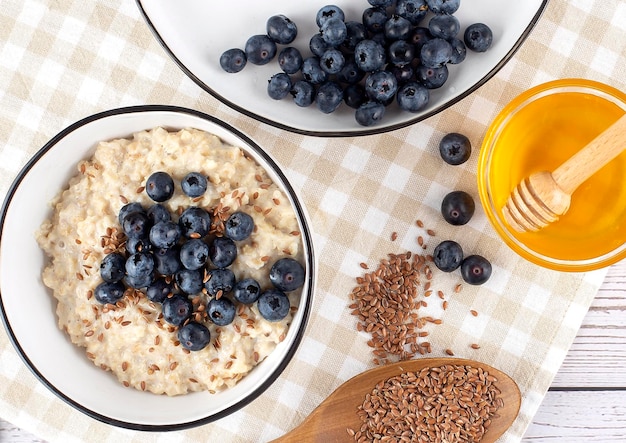 Avena con arándanos en plato con miel y semillas de lino sobre fondo de cuchara de madera para el desayuno en la mañana