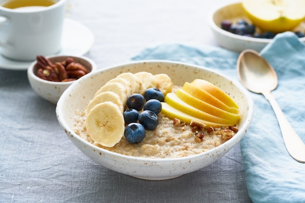 Avena entera, tazón grande de gachas con plátano, arándanos, manzana, nueces. Vista lateral, primer plano