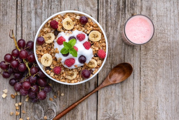 Avena con frambuesas, uvas, plátano y un vaso de yogur sobre un fondo de madera.