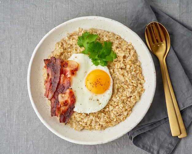 Avena, huevo frito y tocino frito. Desayuno rico en grasas y abundante en calorías, fuente de energía.