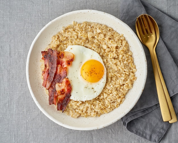 Avena, huevo frito y tocino frito. Desayuno rico en grasas y abundante en calorías, fuente de energía.