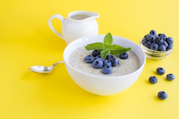 Avena con leche y arándanos en el tazón blanco sobre fondo amarillo Desayuno saludable Copiar espacio