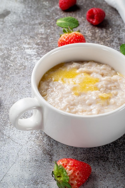 Avena con mantequilla y frambuesas frescas y fresas con menta en una taza blanca contra una mesa de piedra gris. Un desayuno saludable en un restaurante.