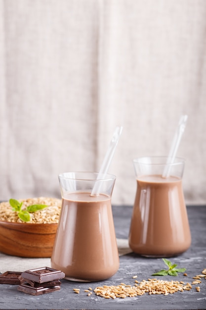 Avena orgánica no láctea chocolate con leche en vidrio y placa de madera con semillas de avena sobre un fondo de hormigón negro