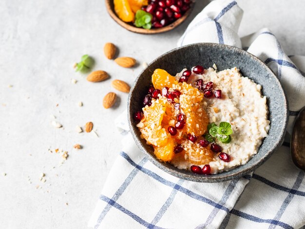 Avena con rodajas de mandarina fresca y semillas de granada, almendras molidas y menta en un recipiente azul sobre fondo blanco.