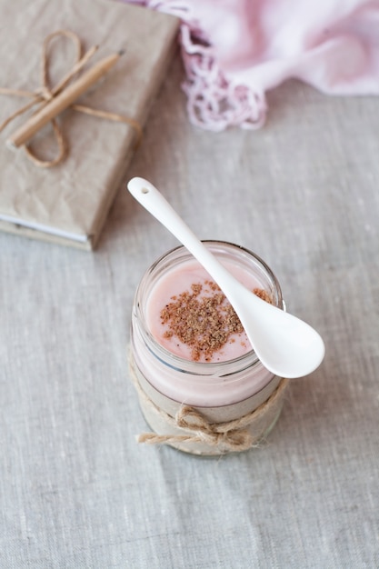 Avena, con sabor a yogur, espolvoreado con canela en un frasco de vidrio. El siguiente es un cuaderno de manualidades y una servilleta rosa.