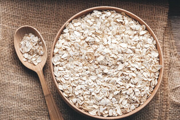 Avena seca en un cuenco de madera y una cuchara sobre un fondo de tela de lino. Copiar, espacio vacío para texto