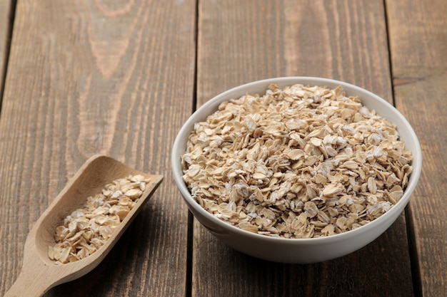 Foto avena seca en un tazón blanco y una cuchara de madera