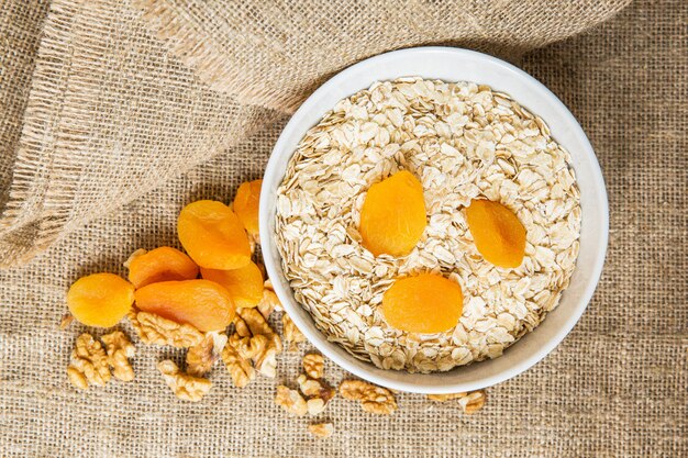 Avena en un tazón blanco con frutas secas y nueces sobre fondo marrón claro de textil