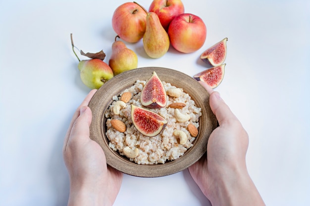 Avena en un tazón con higos frescos, almendras y anacardos Avena con frutas. Las manos de los hombres sostienen un tazón de gachas. Blanco