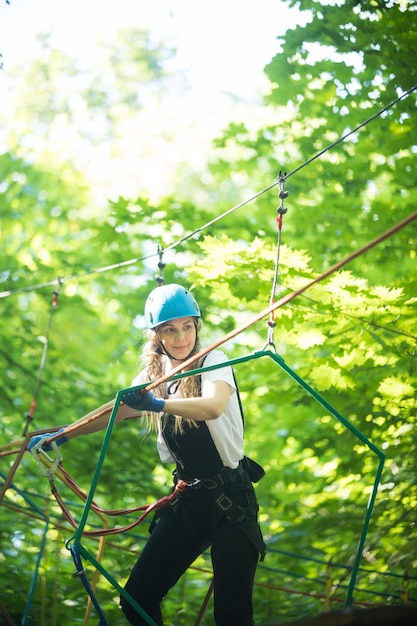 Aventura de cuerda en el bosque mujer con casco azul cruzando el puente de cuerda unido al árbol y mirando directamente