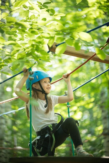 Aventura de cuerda extrema en el bosque una niña parada en el puente de cuerda y sonriendo mirando hacia arriba