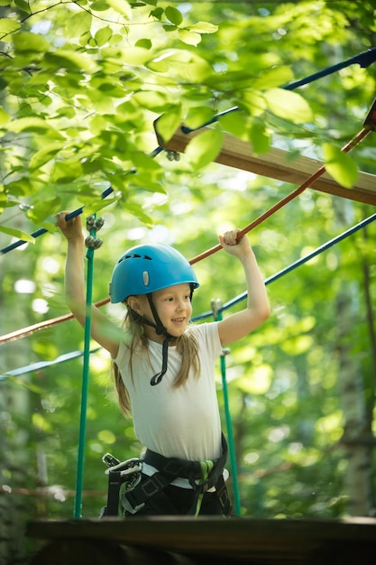 Aventura de cuerda extrema en el bosque una niña parada en el puente de cuerda y sonriendo