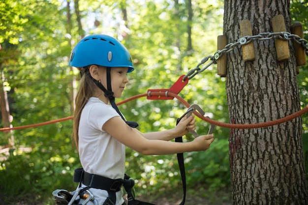 Aventura de cuerda en el parque una niña pequeña con un gancho de seguro atado a la cuerda caminando hacia el área