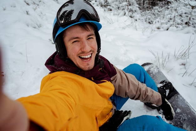 Aventura para esportes de inverno. Homem de snowboarder, caminhadas na montanha e fazendo selfie. Procurando pó para freeride.