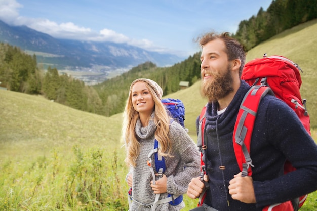 Aventura, viagens, turismo, caminhada e conceito de pessoas - casal sorridente andando com mochilas sobre fundo de paisagem natural