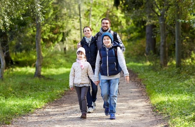 Foto aventura, viagens, turismo, caminhada e conceito de pessoas - família feliz andando com mochilas na floresta