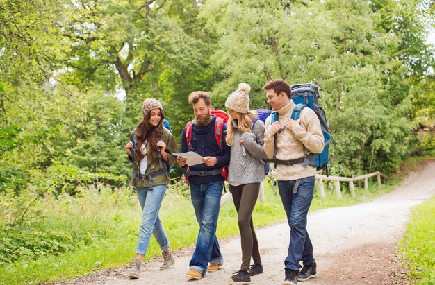 aventura, viagens, turismo, caminhada e conceito de pessoas - grupo de amigos sorridentes andando com mochilas e mapa caminhando ao ar livre