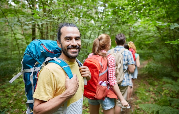 aventura, viagens, turismo, caminhada e conceito de pessoas - grupo de amigos sorridentes andando com mochilas na floresta