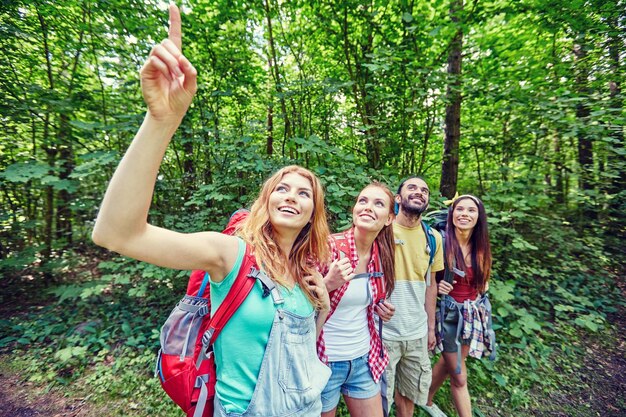 aventura, viagens, turismo, caminhada e conceito de pessoas - grupo de amigos sorridentes com mochilas apontando o dedo para cima na floresta