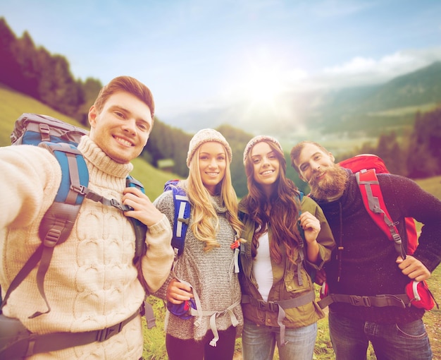 aventura, viagens, turismo, caminhada e conceito de pessoas - grupo de amigos sorridentes com mochilas fazendo selfie sobre fundo de montanhas e colinas alpinas