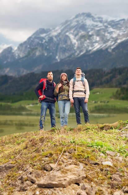 Aventura, viagens, turismo, caminhada e conceito de pessoas - grupo de amigos sorridentes com mochilas sobre fundo de montanhas