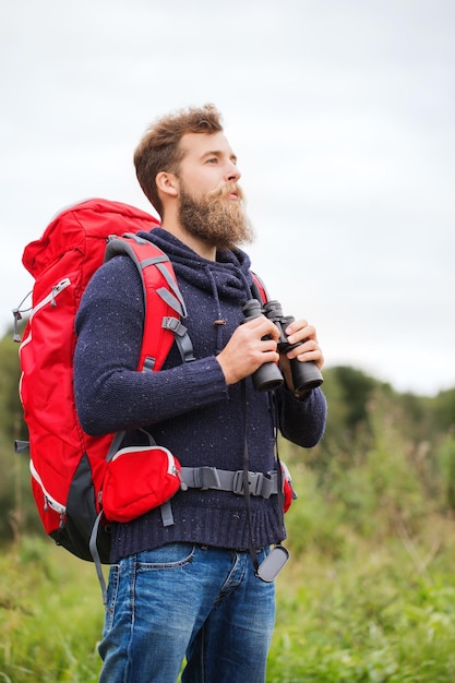 aventura, viagens, turismo, caminhada e conceito de pessoas - homem com mochila vermelha e binóculo ao ar livre