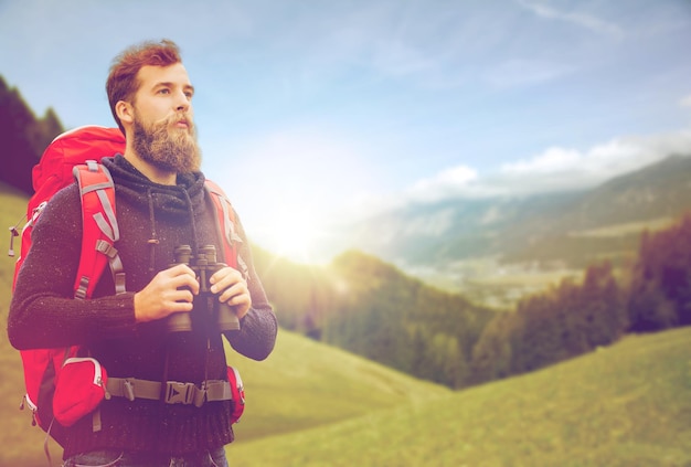 aventura, viagens, turismo, caminhada e conceito de pessoas - homem com mochila vermelha e binóculo sobre fundo alpino de montanhas e colinas