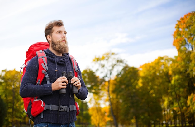 aventura, viagens, turismo, caminhada e conceito de pessoas - homem com mochila vermelha e binóculo sobre fundo natural