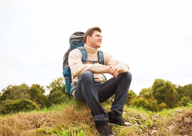 Aventura, viagens, turismo, caminhada e conceito de pessoas - homem sorridente com mochila sentada no chão