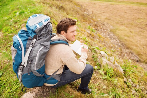 aventura, viagens, turismo, caminhada e conceito de pessoas - homem sorridente com mochila sentada no chão