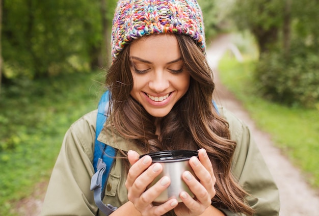 aventura, viagens, turismo, caminhada e conceito de pessoas - jovem sorridente com copo e mochila na floresta