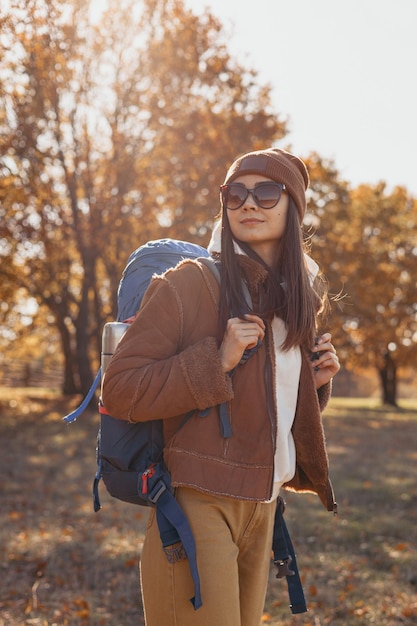 Aventureira sorridente com mochila parada na natureza no outono em dia ensolarado