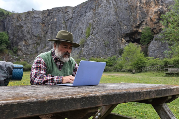 Aventureiro masculino mochileiro e chapéu usando laptop em um vale nas montanhas