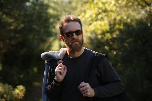 Aventurero hombre caucásico barbudo con gafas de sol posando en la naturaleza