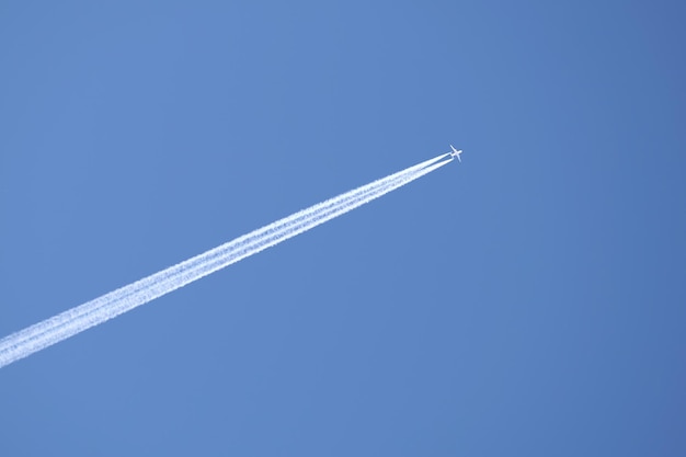 Avião a jato de passageiros distante voando em alta altitude no céu azul claro, deixando um rastro de fumaça branca de rastos para trás. Conceito de transporte aéreo.