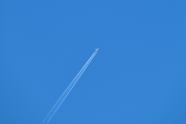 Avião a jato de passageiros distante voando em alta altitude no céu azul claro deixando um rastro de fumaça branca para trás. Conceito de transporte aéreo